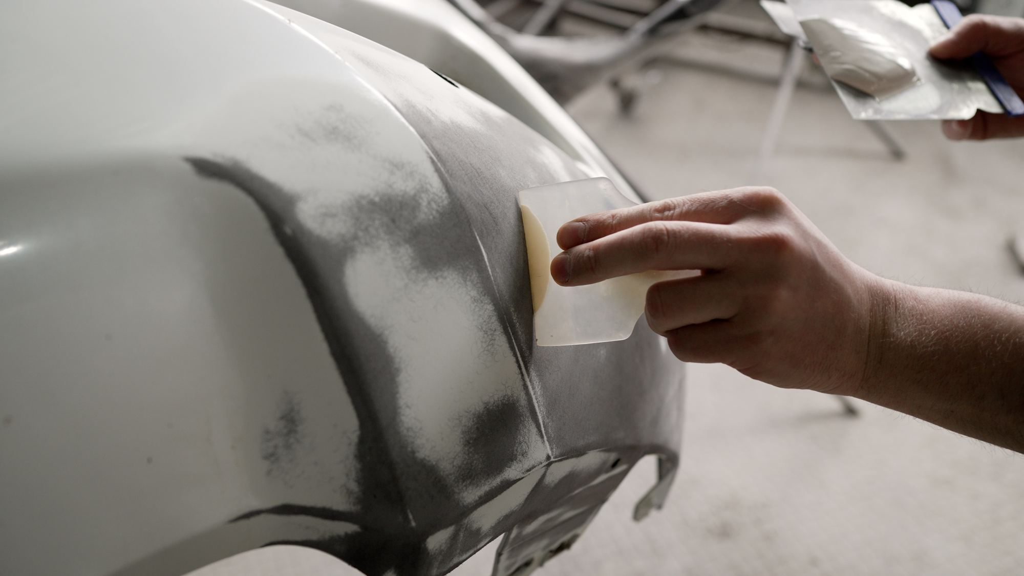 Panel beater applying body filler to a car panel during collision repair