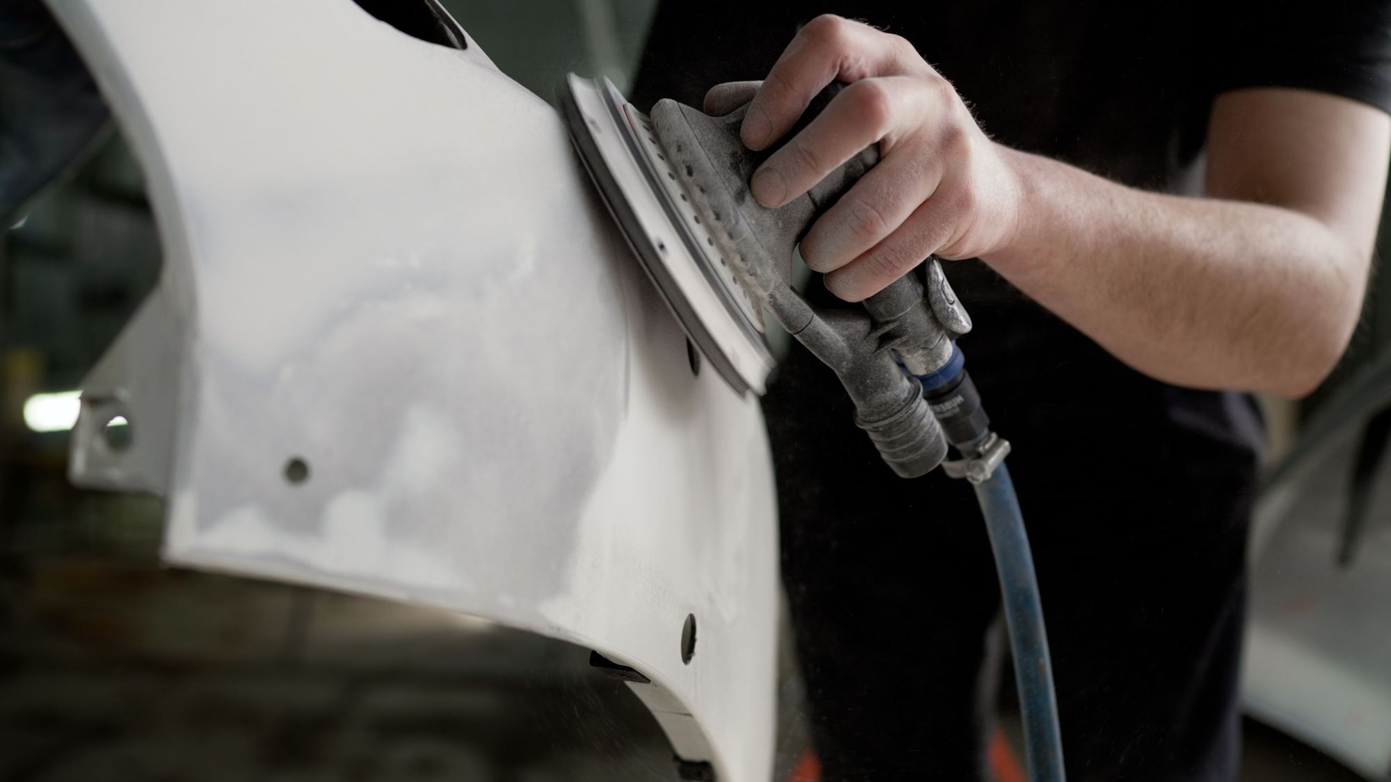 Orbital sander preparing a white bumper for paint