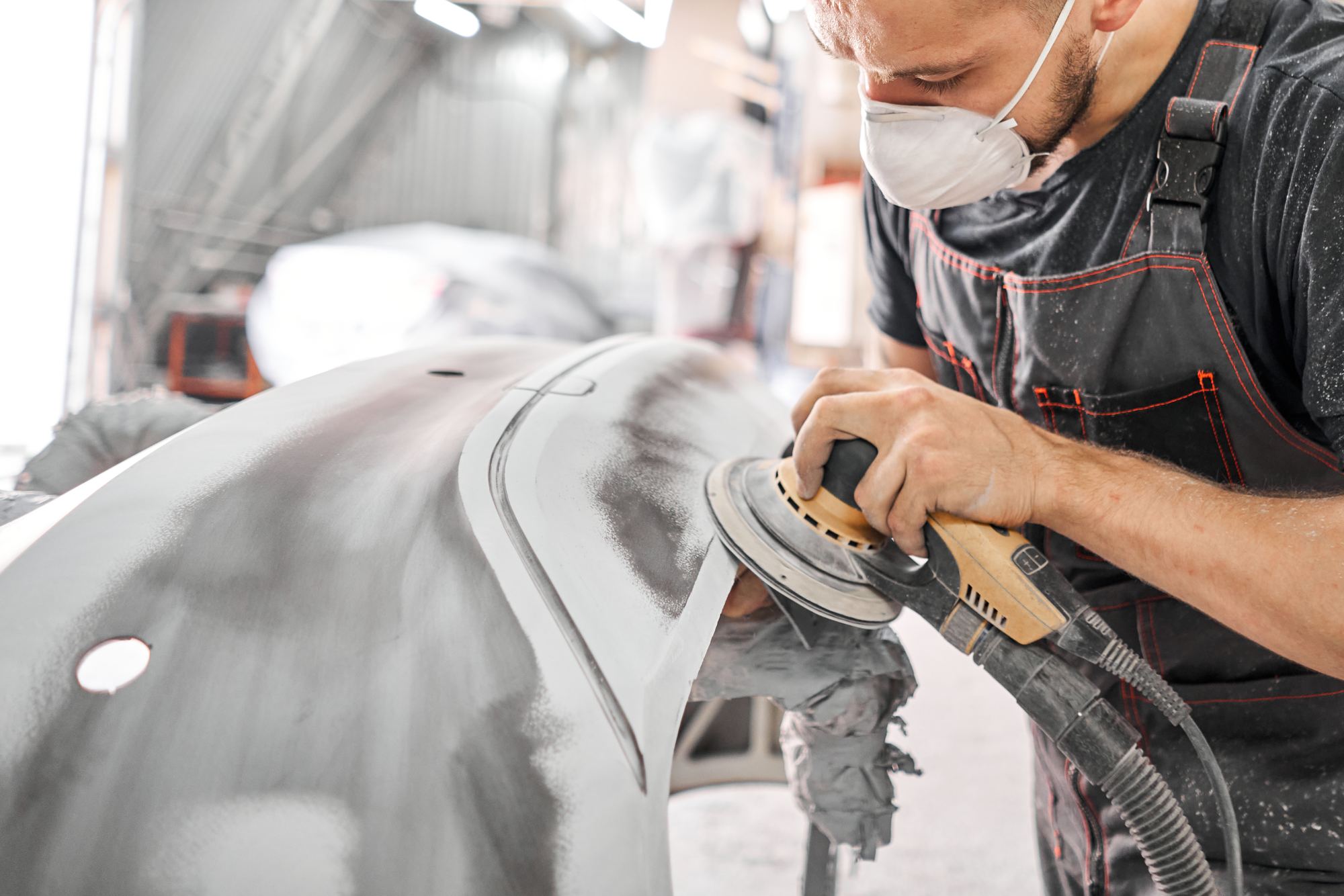 Panel beater in a mask sanding a car panel before spray painting